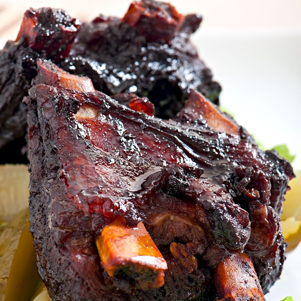 Close-up of Fisher's BBQ & Moore's dark, glistening BBQ ribs with visible bones.