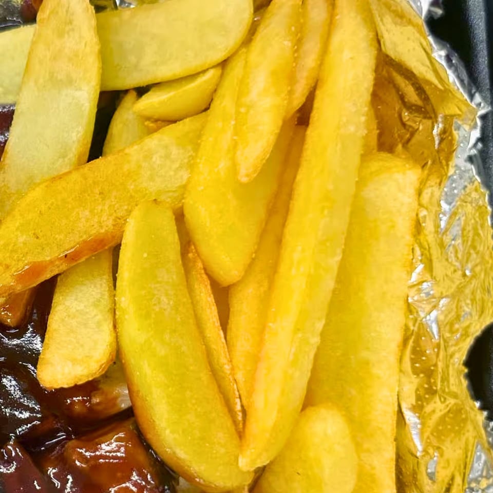 Close-up of golden french fries next to barbecue ribs in a foil container from Fisher's BBQ & Moore.