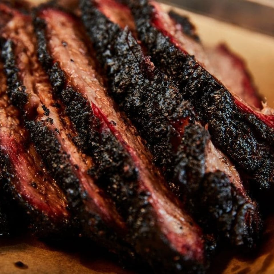 Close-up of sliced, smoked brisket with a dark, peppery bark and a pink smoke ring.