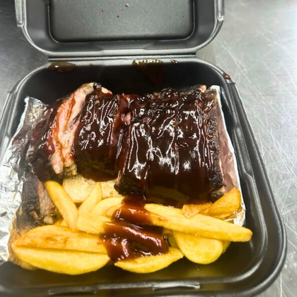 Fisher's BBQ & Moore ribs and fries in a black takeout container, covered in rich BBQ sauce.