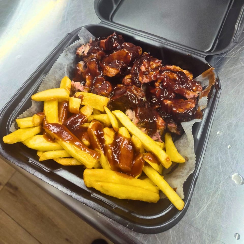 Fisher's BBQ & Moore's BBQ ribs and fries, drizzled with sauce, in a takeout container.