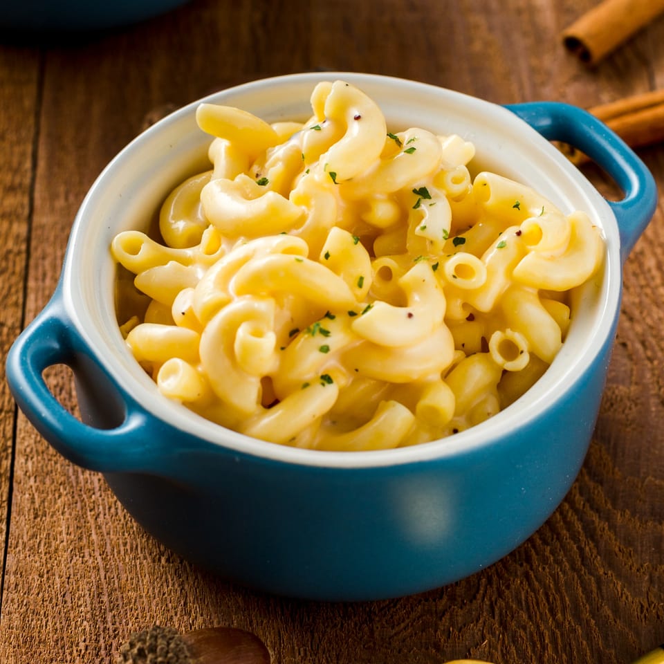 Creamy macaroni and cheese, garnished with parsley, in a blue ceramic bowl on a wooden table.