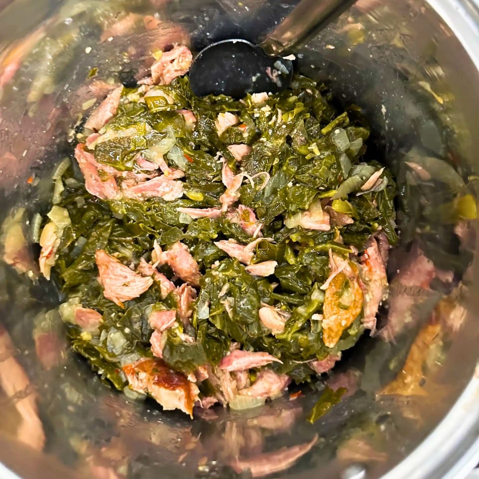 Close-up of Fisher's BBQ & Moore's collard greens with smoked turkey in a metal pot.